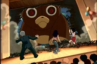 The teddy bear breaks through the gym wall, terrifying Mr. Delmas, Sissi, and the students present at the Annual School Prom.